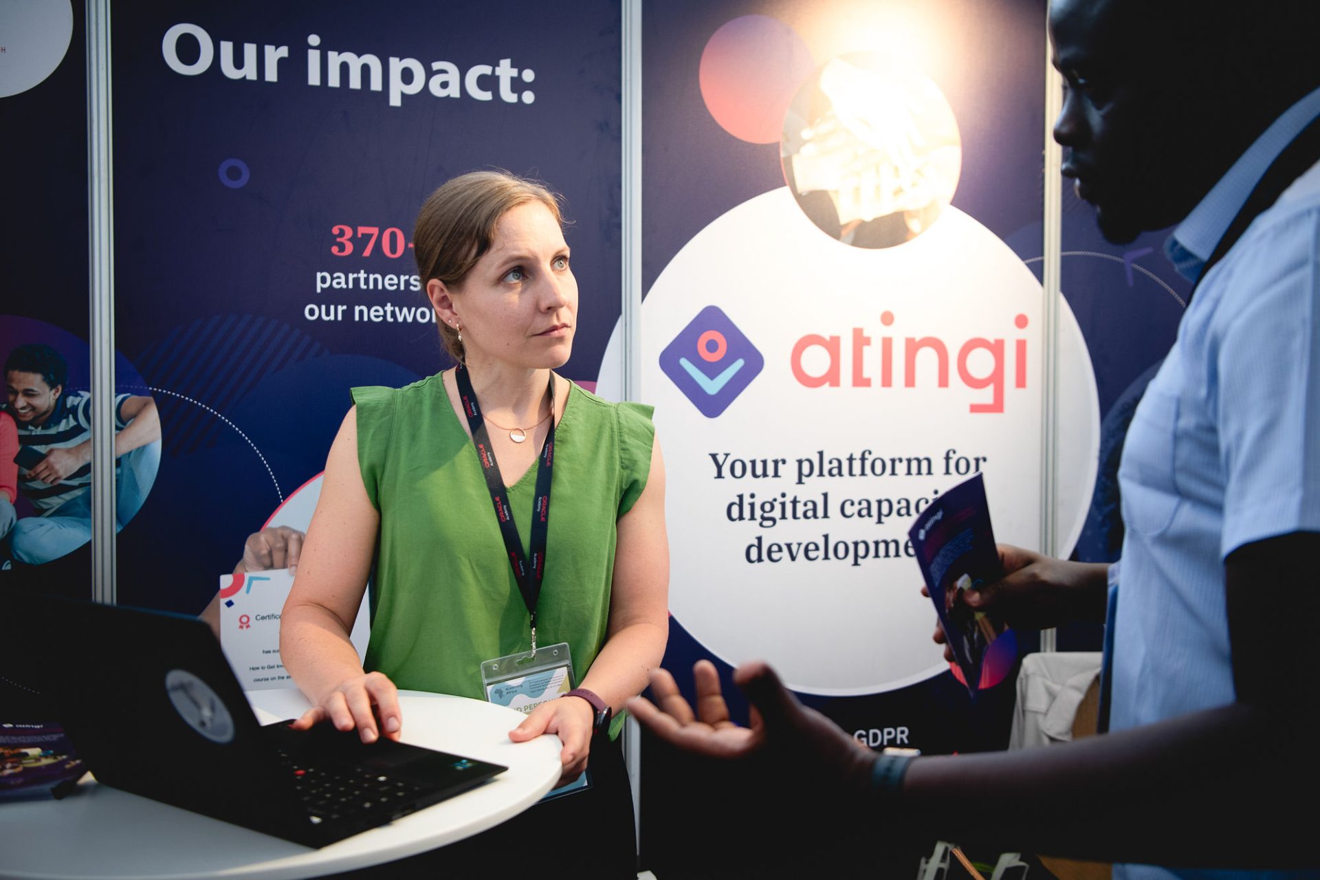 Woman in green blouse standing at a conference booth at a laptop.